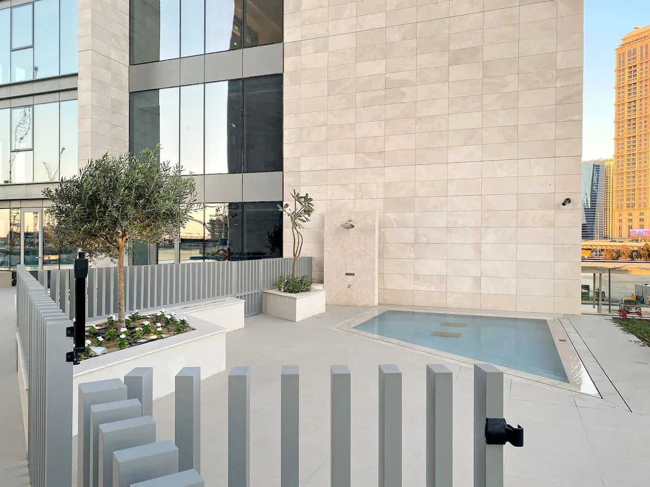 A modern building terrace with a shallow rectangular pool and planted trees.