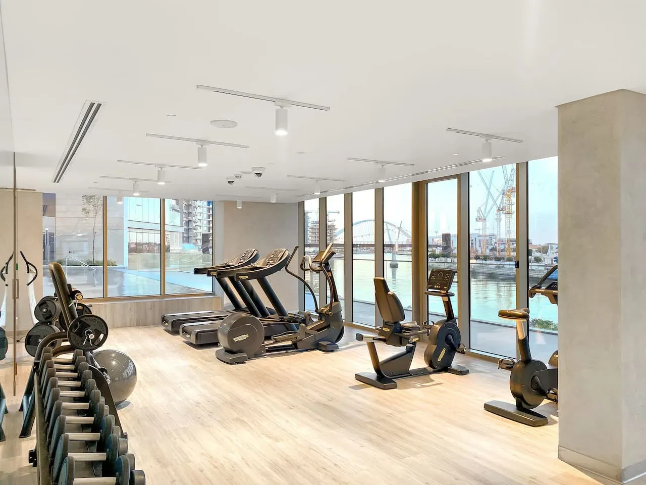 A bright gym with rows of exercise equipment beside large windows.