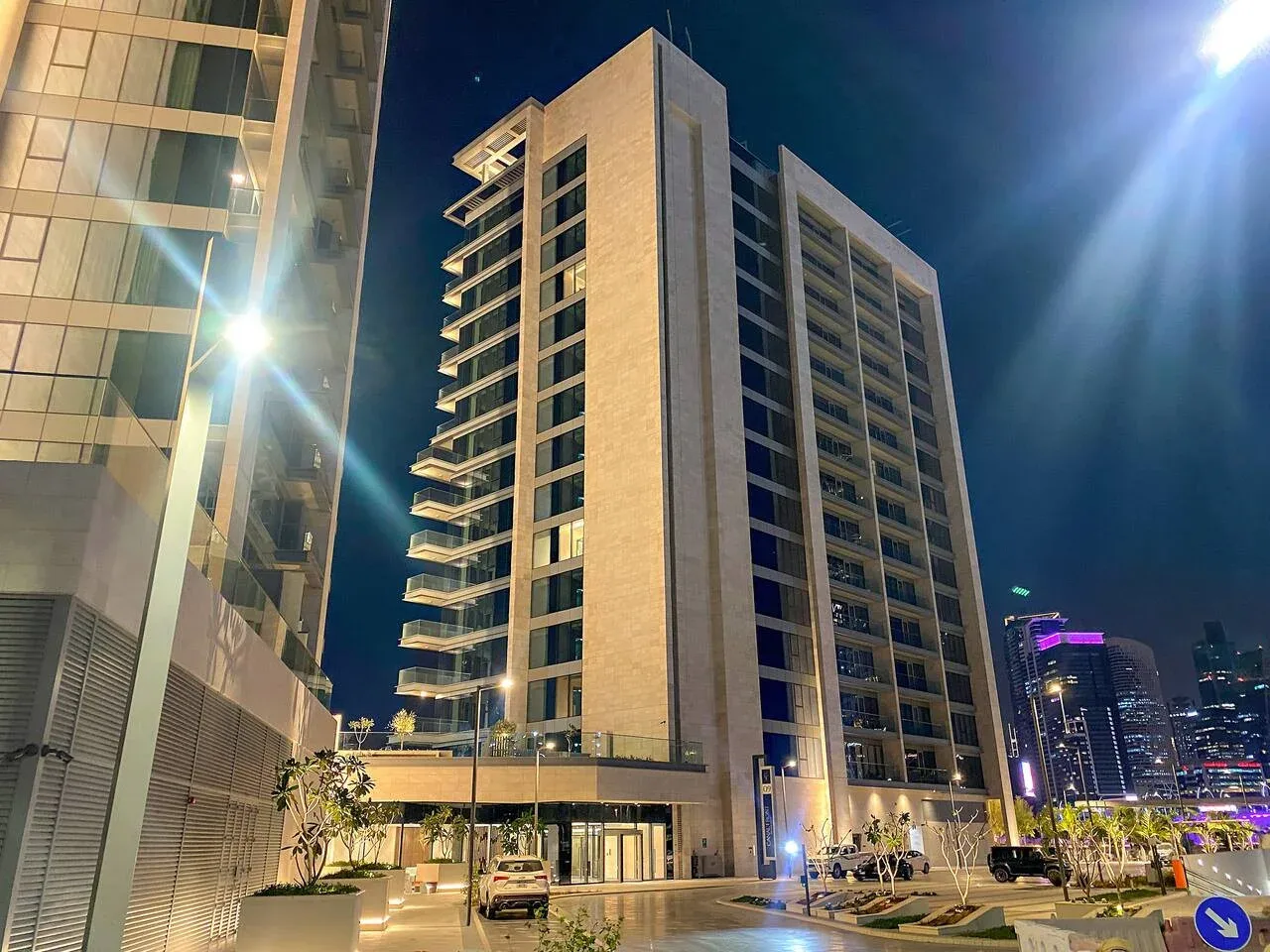 A high-rise building stands beside a lit entrance plaza at night.