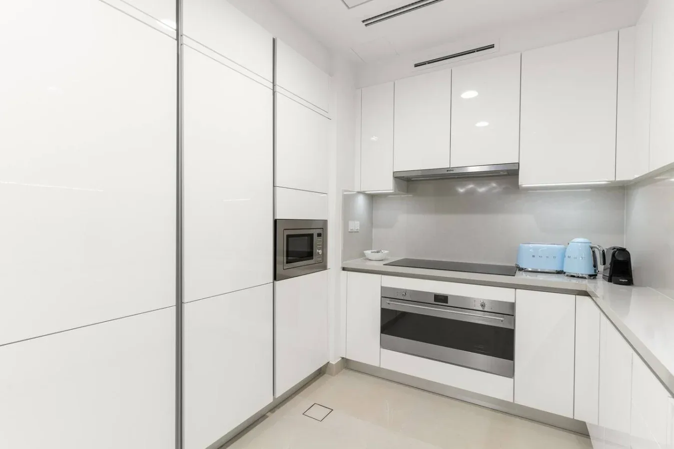A bright modern kitchen with white cabinets, a built-in oven, and a cooktop.