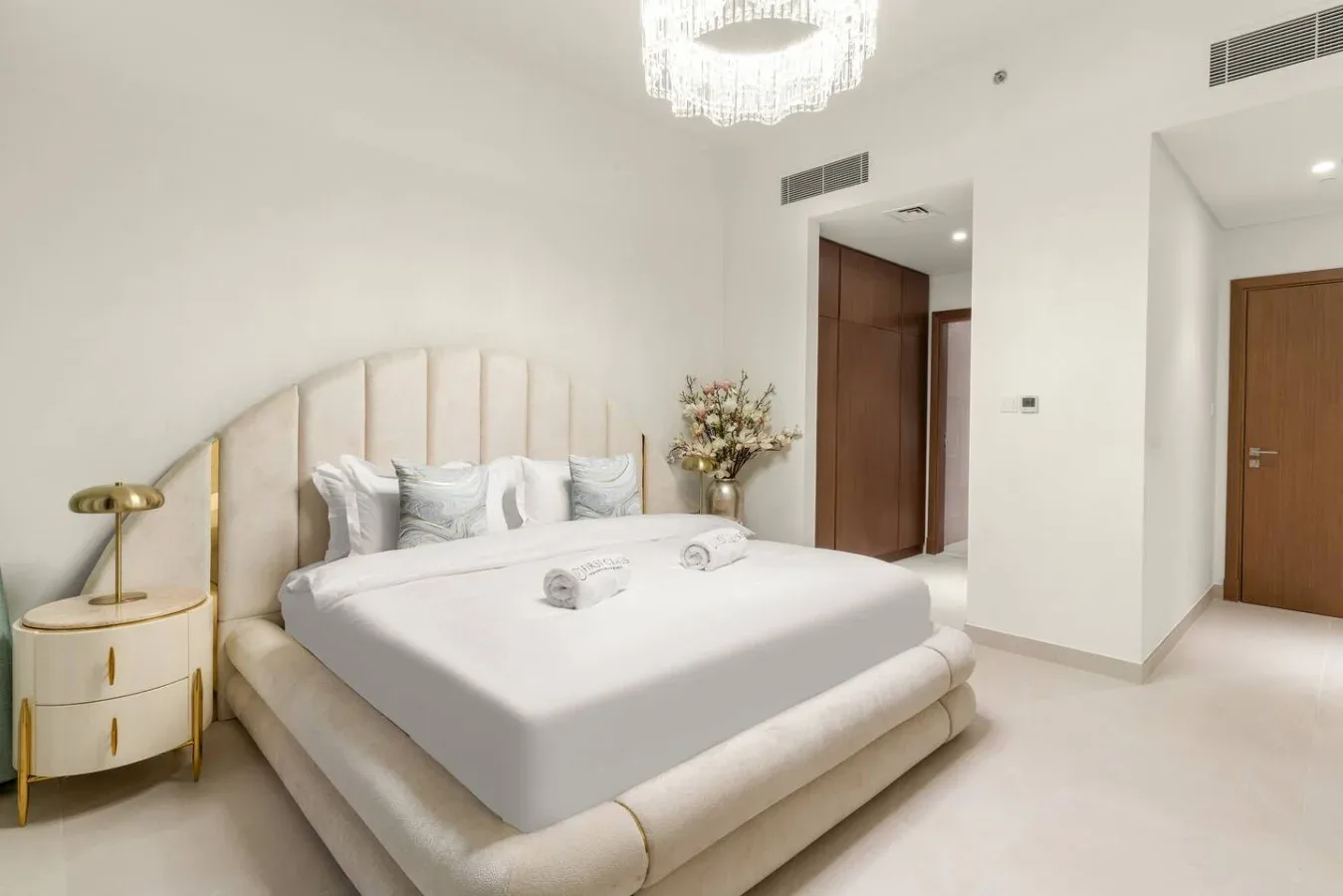 A bright bedroom with a large bed, bedside table, and chandelier.