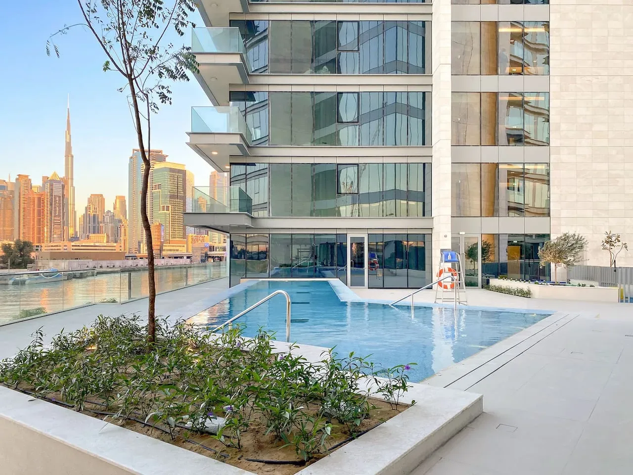 A rooftop pool beside a modern building overlooks the waterfront and city skyline.