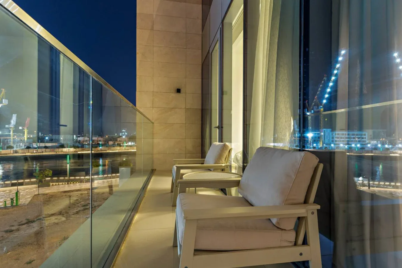 A balcony seating area overlooks a brightly lit city at night.