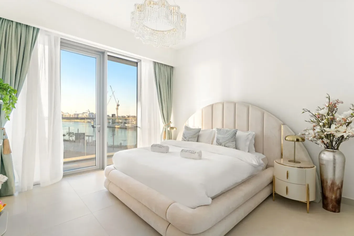 A bright bedroom with a bed beside floor-to-ceiling windows overlooking the water.