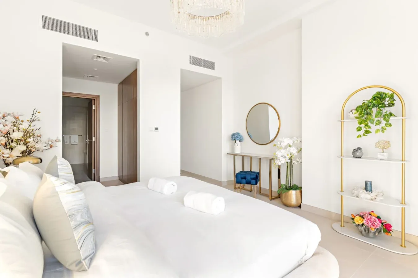 A bright bedroom with a white bed, a round mirror, and decorative shelving.