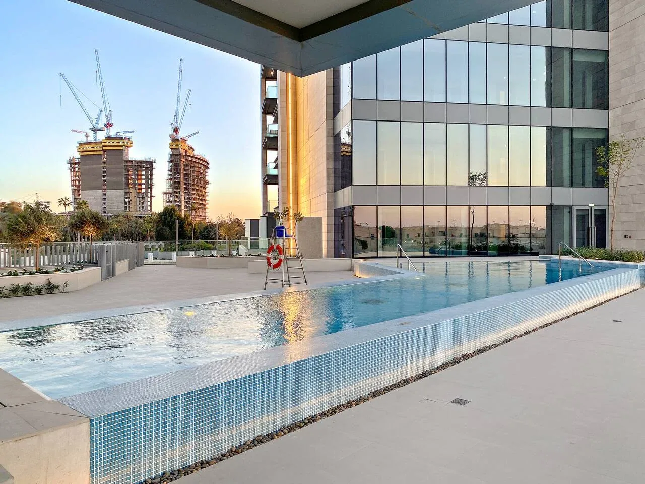 An outdoor swimming pool beside a modern glass-fronted building.
