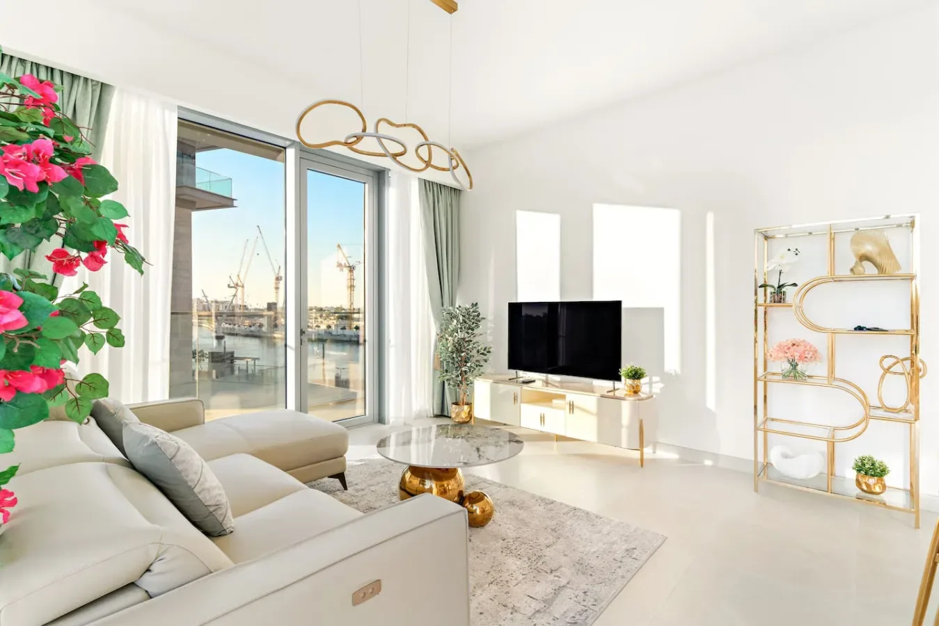 A bright living room with seating, a television, and large windows overlooking the water.