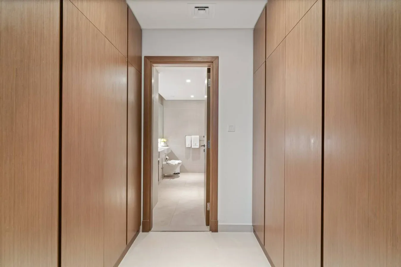 A hallway lined with built-in wooden cabinets leads to a bright room.