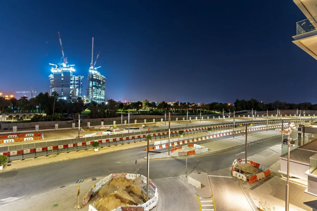 A nighttime city construction site with illuminated high-rise buildings in the background.