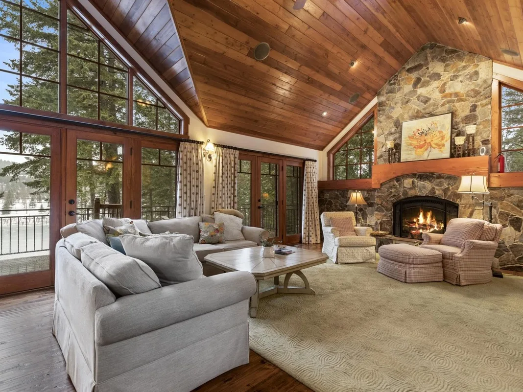 A living room with a seating area, large windows, and a stone fireplace.