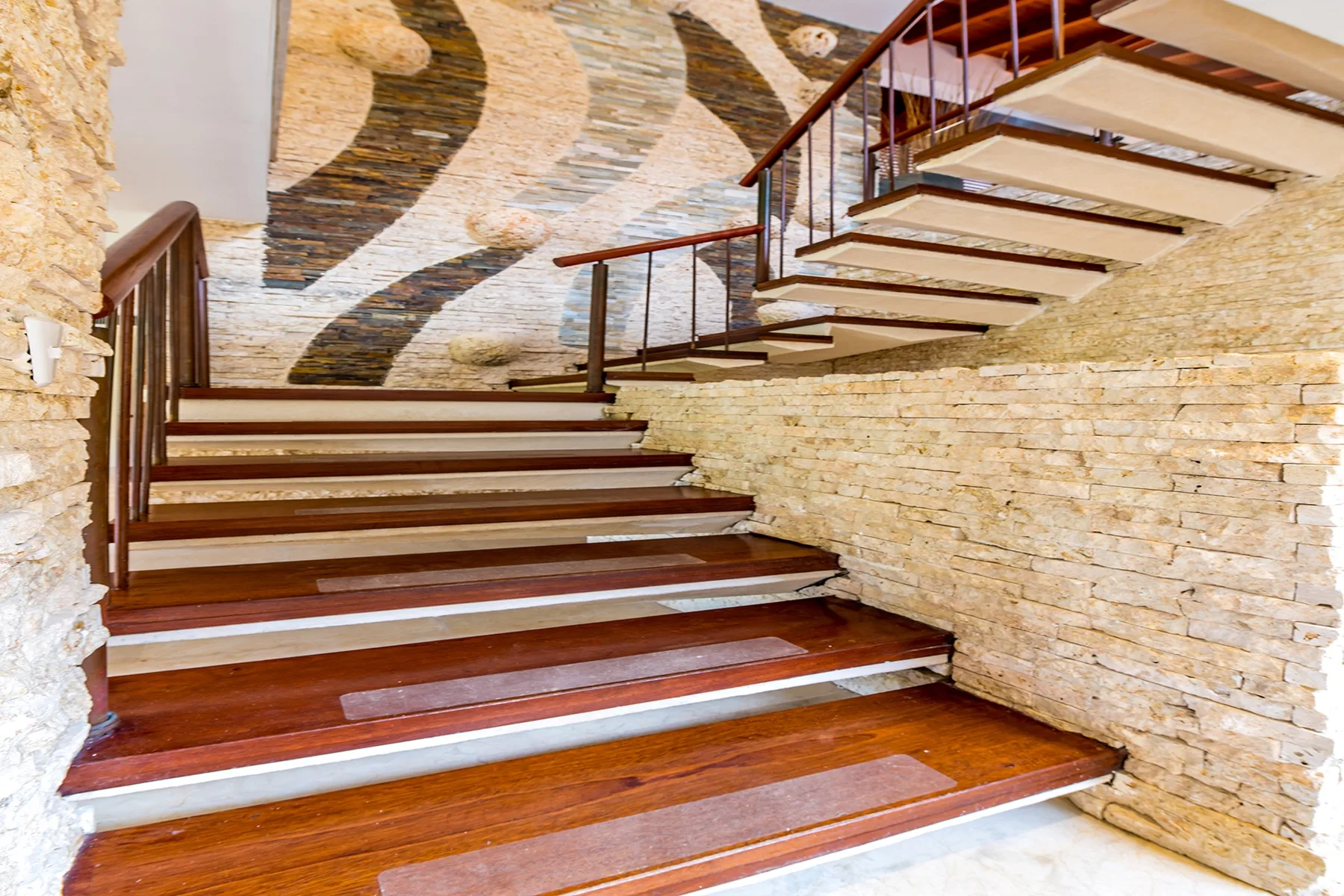 Una escalera interior con peldaños de madera, barandillas metálicas y paredes de piedra.