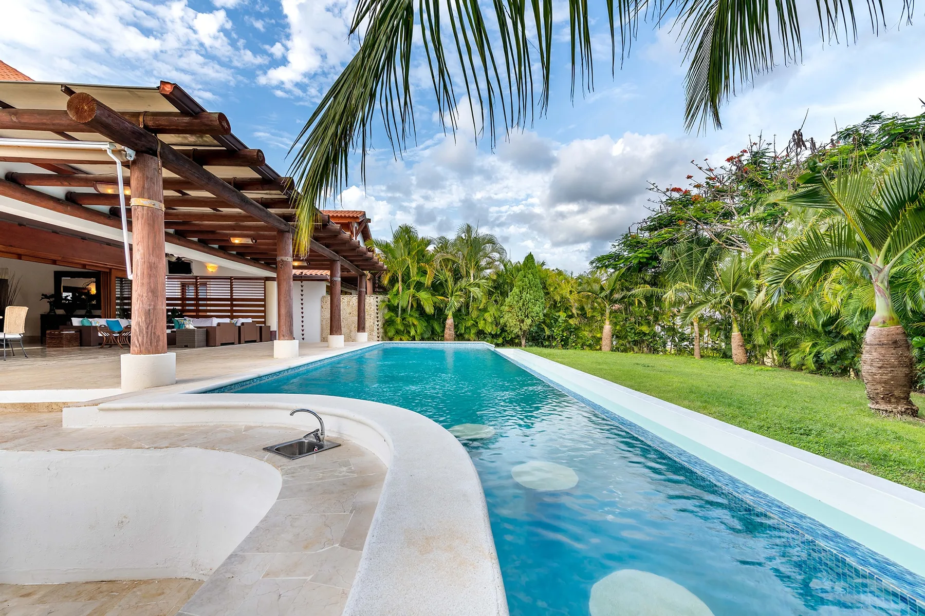Una piscina al aire libre junto a un patio cubierto y vegetación tropical.