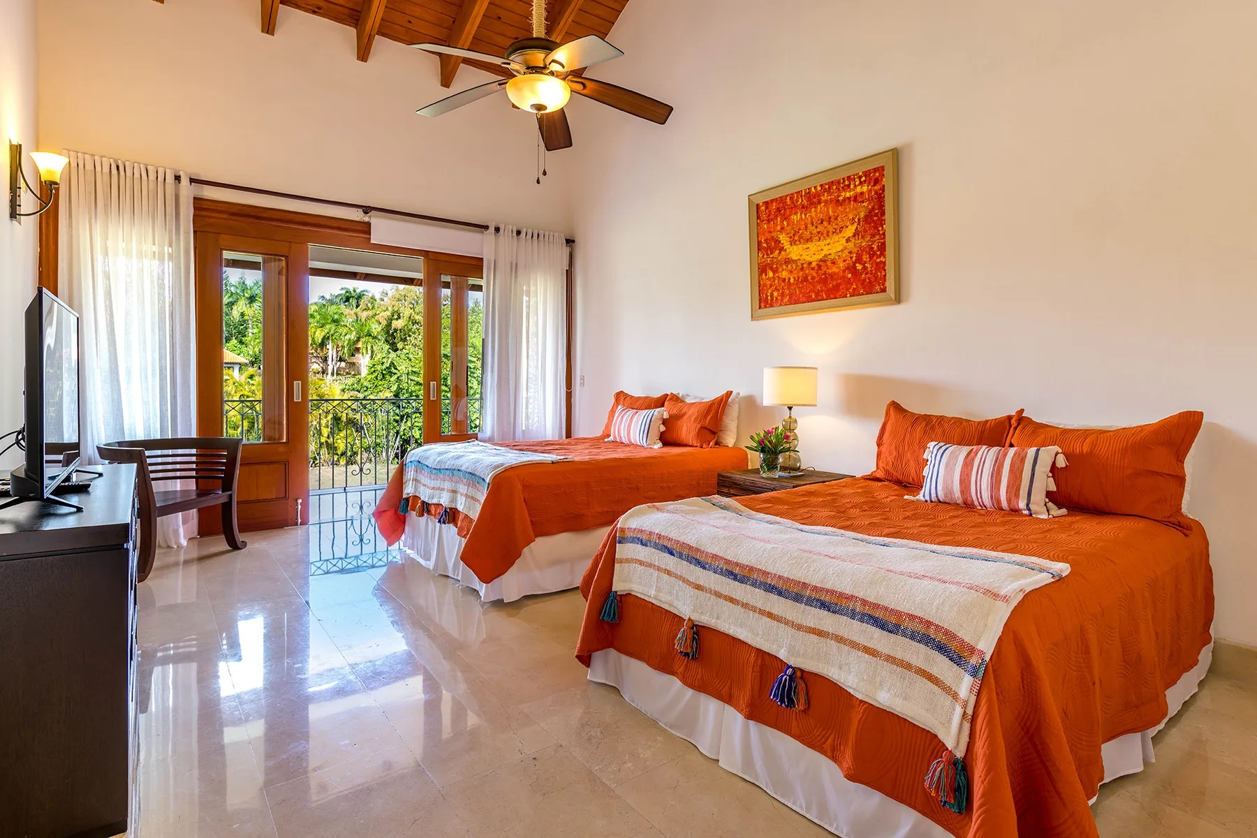 Un dormitorio luminoso con dos camas vestidas de naranja y puertas de vidrio que dan a un balcón.
