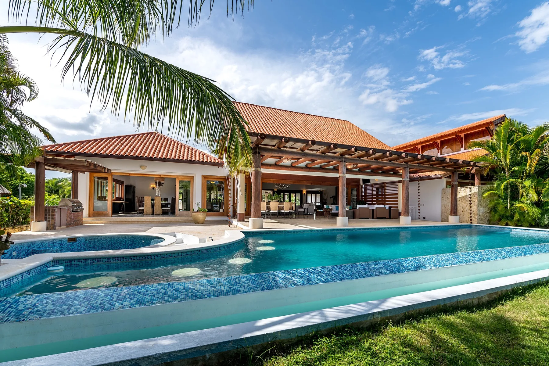 Una gran piscina al aire libre está frente a una villa con techo de tejas.
