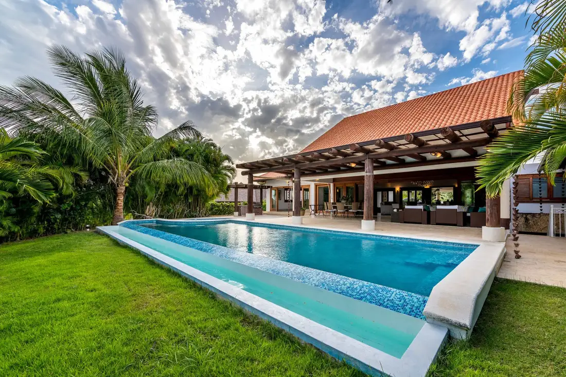 Una piscina al aire libre junto a un patio cubierto y césped verde.