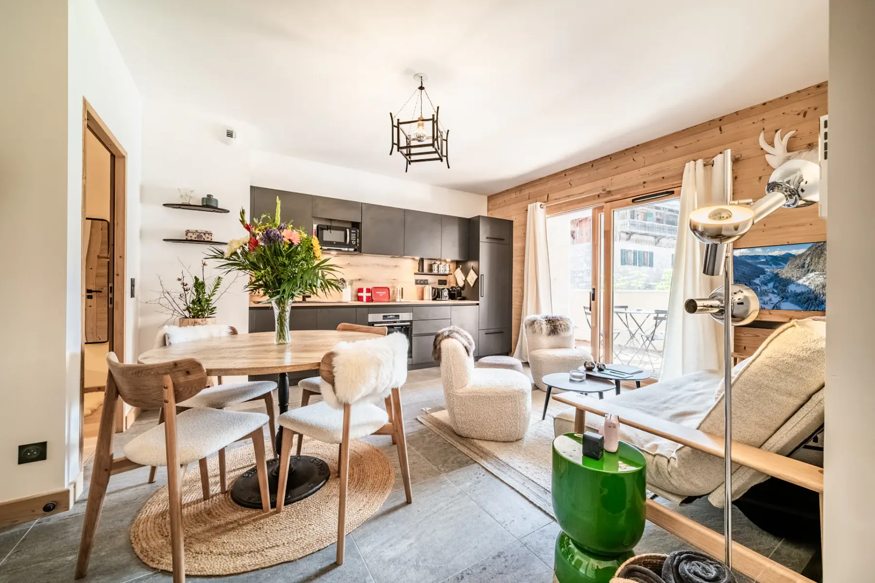 Acogedora sala de estar y cocina de planta abierta con decoración rústica, una mesa de comedor redonda, cocina moderna y zona de asientos junto a una ventana grande.