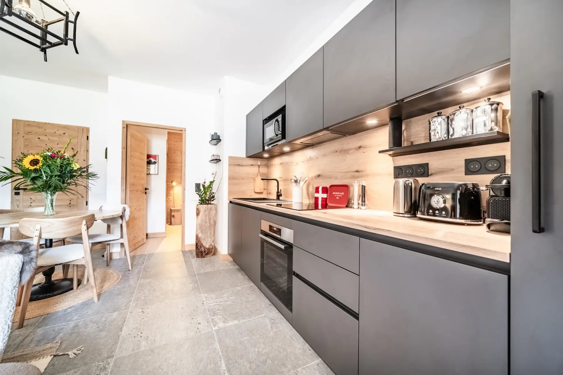 Cocina y comedor de planta abierta con gabinetes oscuros y una mesa redonda.