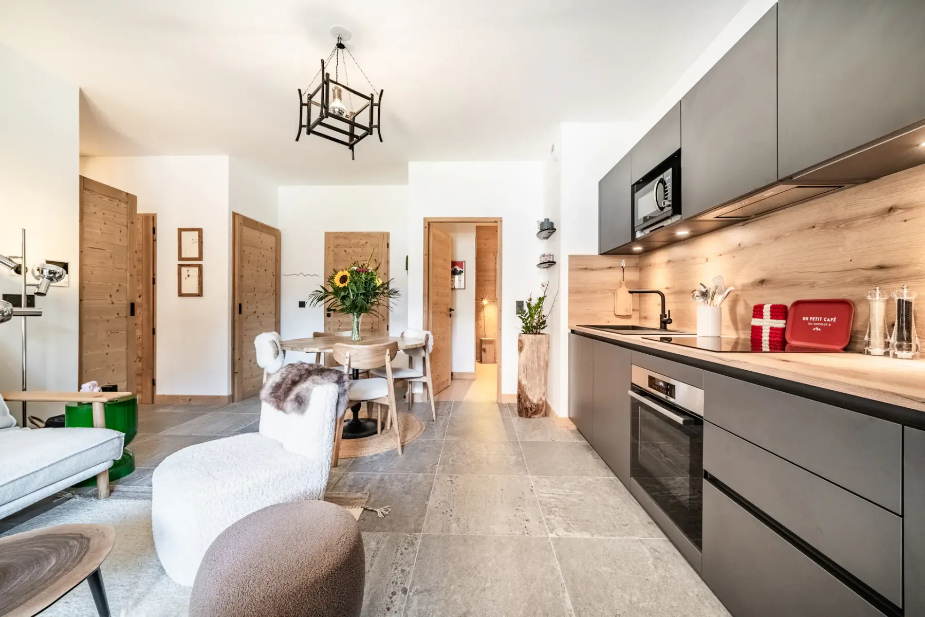 Acogedora sala de estar y cocina de planta abierta con decoración rústica, una mesa de comedor redonda, cocina moderna y zona de asientos junto a una ventana grande.