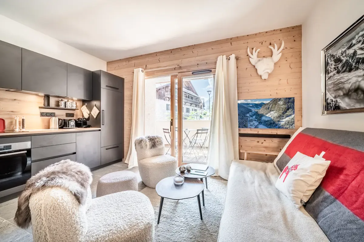 A bright open-plan living area with a compact kitchen, seating, and a balcony.