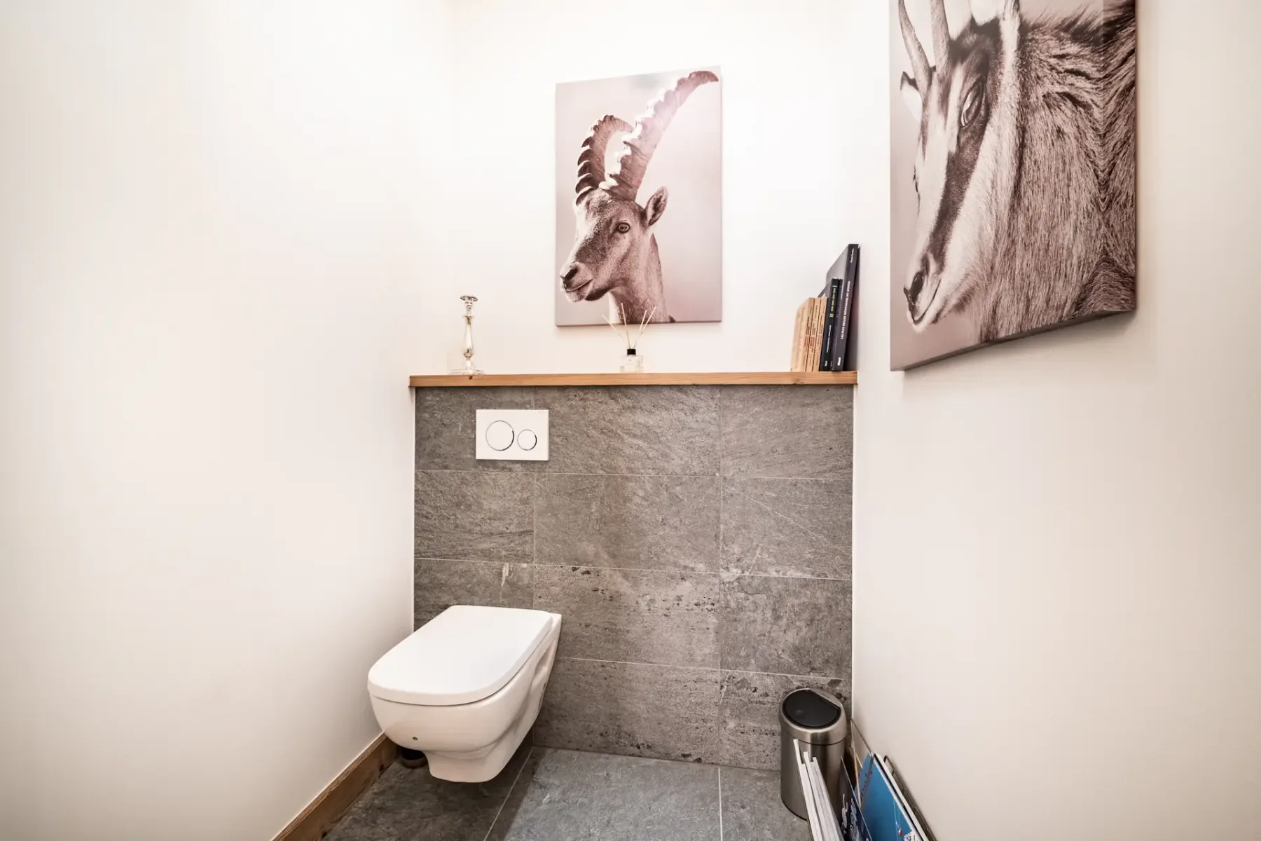 Baño minimalista con un inodoro suspendido, un revestimiento de azulejos grises y obras de arte de temática animal en las paredes.