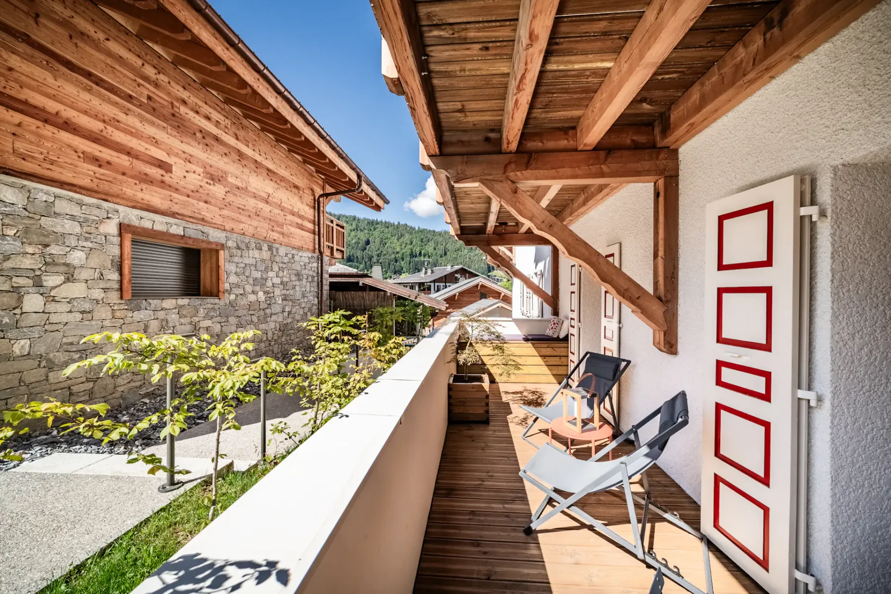 Balcón de madera con asientos y vistas a edificios cercanos y una ladera verde.