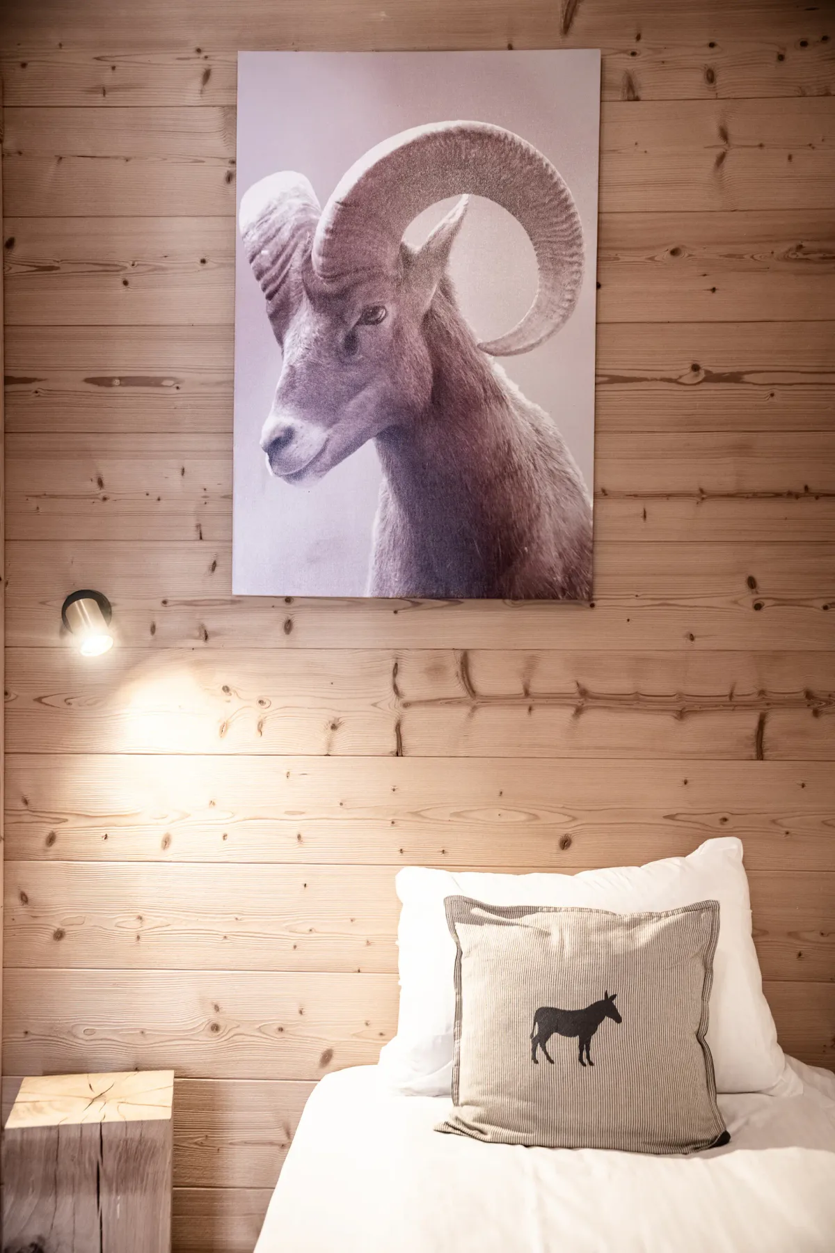 Una cama está junto a una pared revestida de madera, bajo un gran retrato de un carnero.