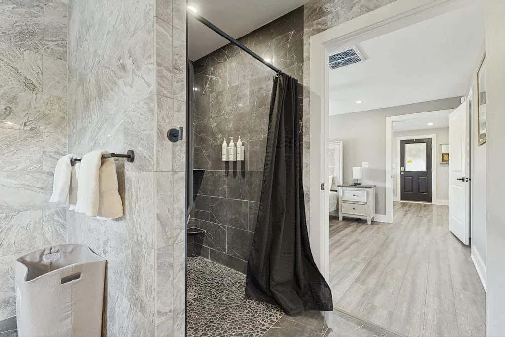 Un baño con una ducha revestida de azulejos y una puerta abierta a un pasillo luminoso.