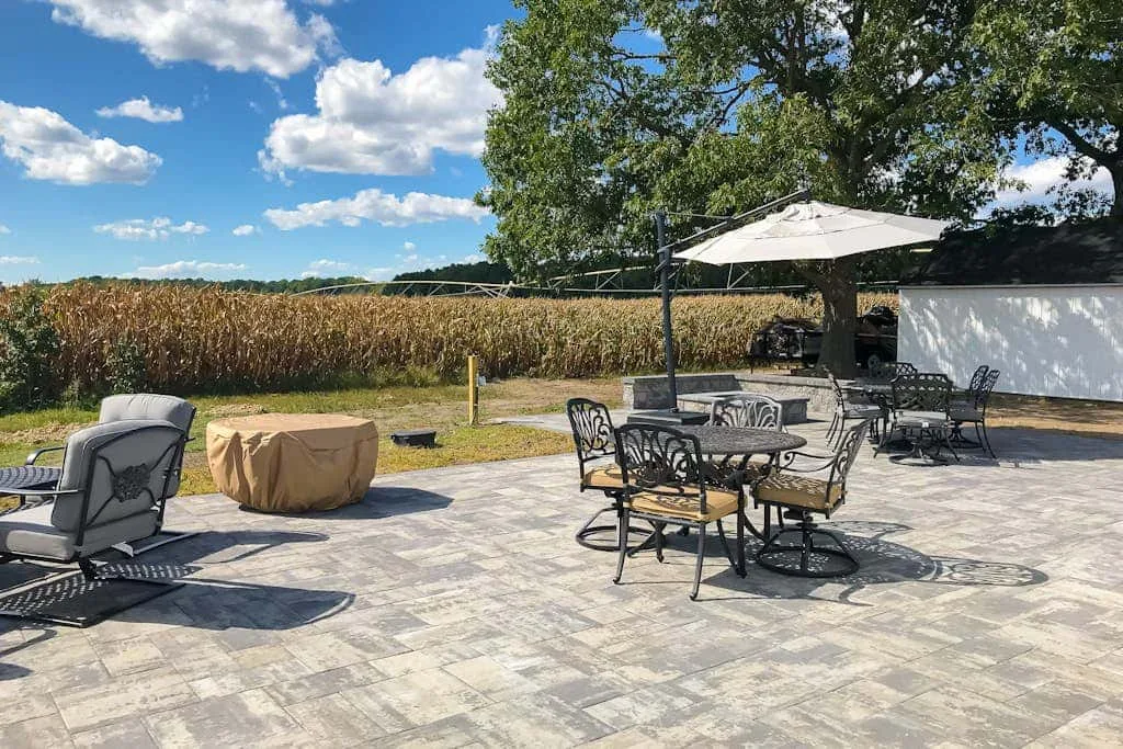 Un patio al aire libre con asientos para comer, sillones y una sombrilla junto a un campo.