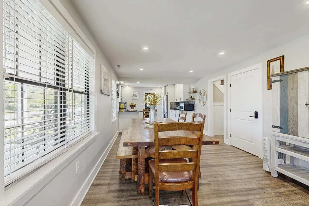 Un comedor con una mesa de madera y sillas junto a grandes ventanas.