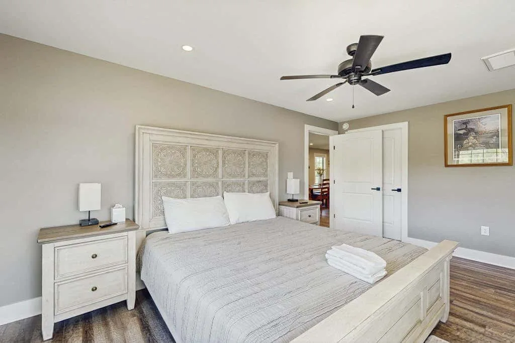 Un dormitorio con una cama grande, ropa de cama blanca y un ventilador de techo.