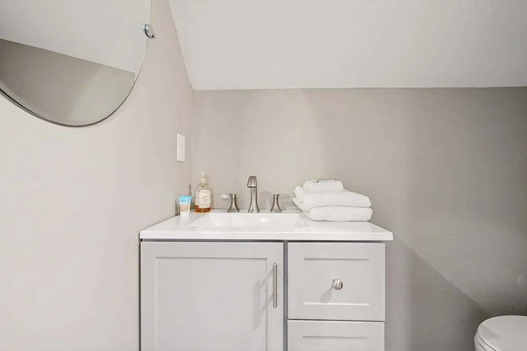 Un tocador de baño con toallas dobladas y artículos de aseo bajo un espejo.