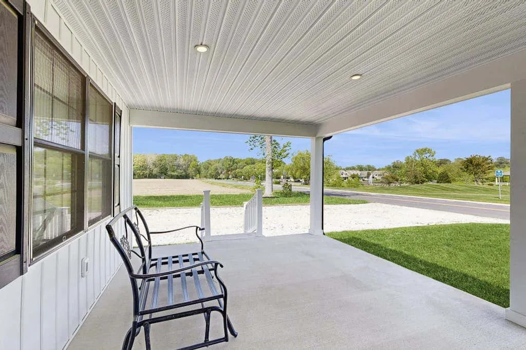 A covered porch with black seating overlooks a grassy lawn and road.