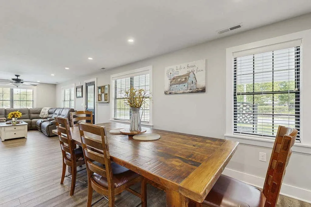 Un comedor con una mesa de madera y asientos junto a varias ventanas.