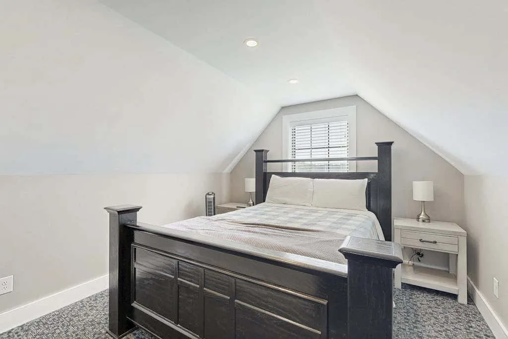 Un dormitorio con una cama grande bajo un techo inclinado y una ventana.