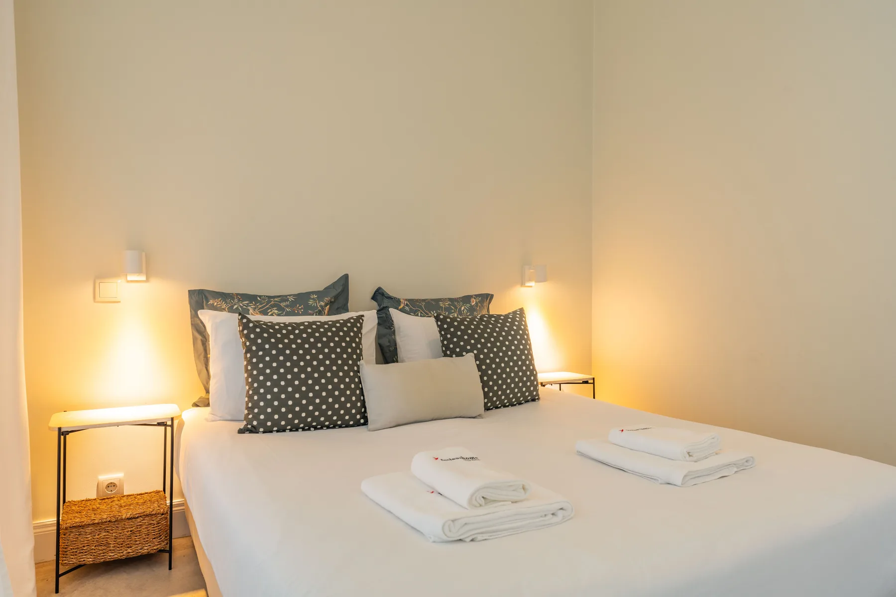 Un dormitorio con una cama bien arreglada, almohadas estampadas y mesitas de noche.