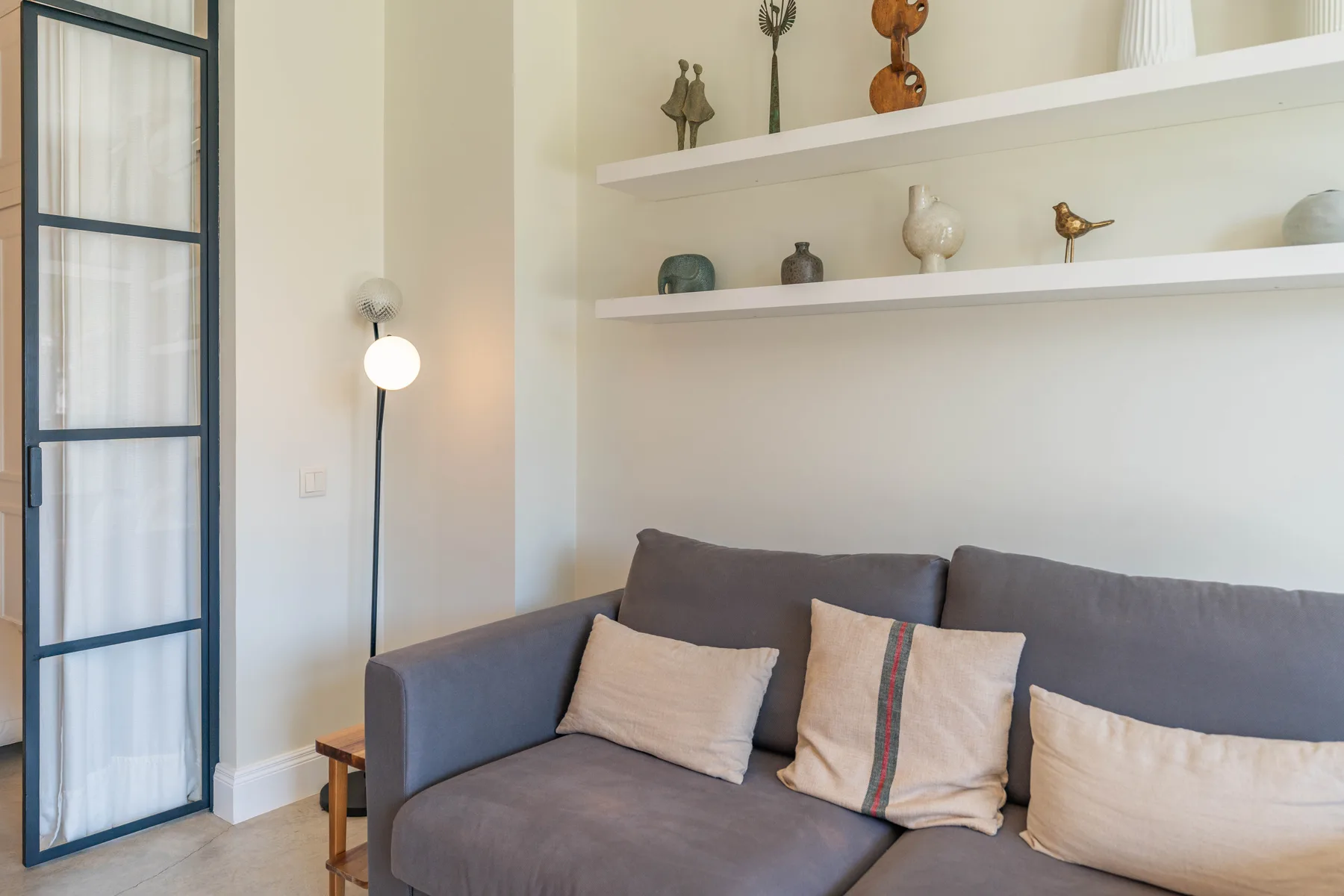 Una sala de estar con un sofá gris y objetos decorativos en estantes.