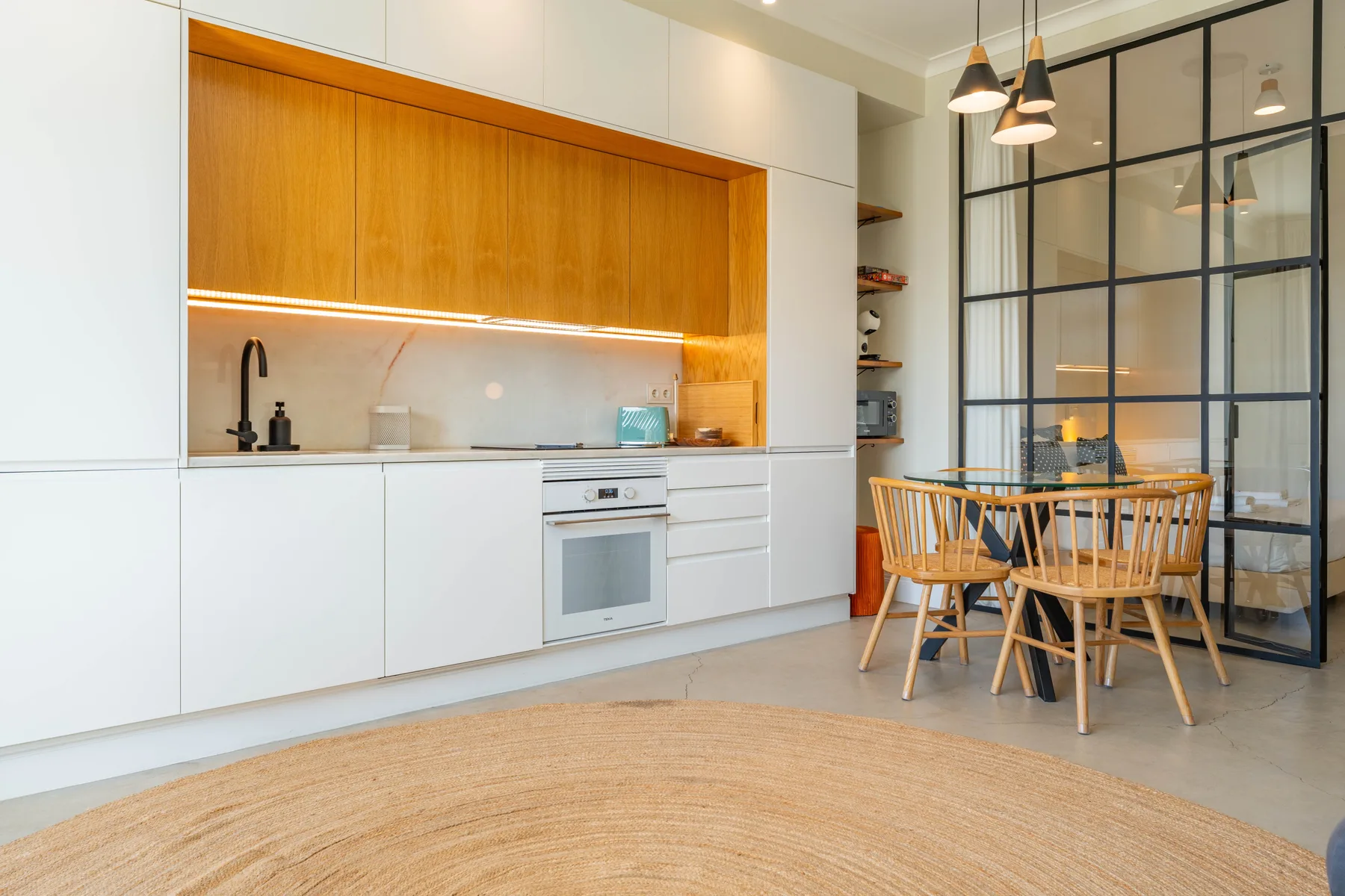 Una cocina moderna y zona de comedor con una mesa redonda junto a una mampara de vidrio.