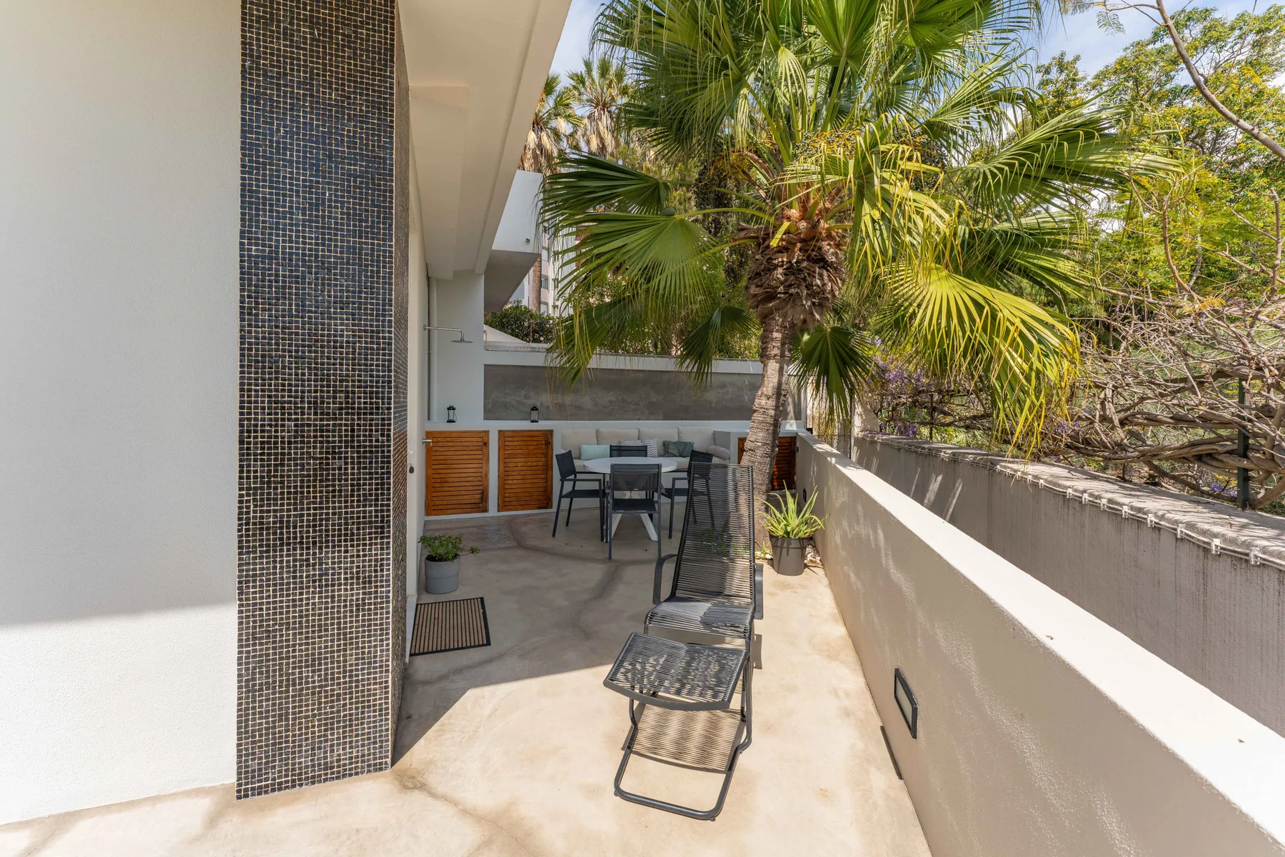 Una terraza soleada con asientos al aire libre, una tumbona y palmeras.