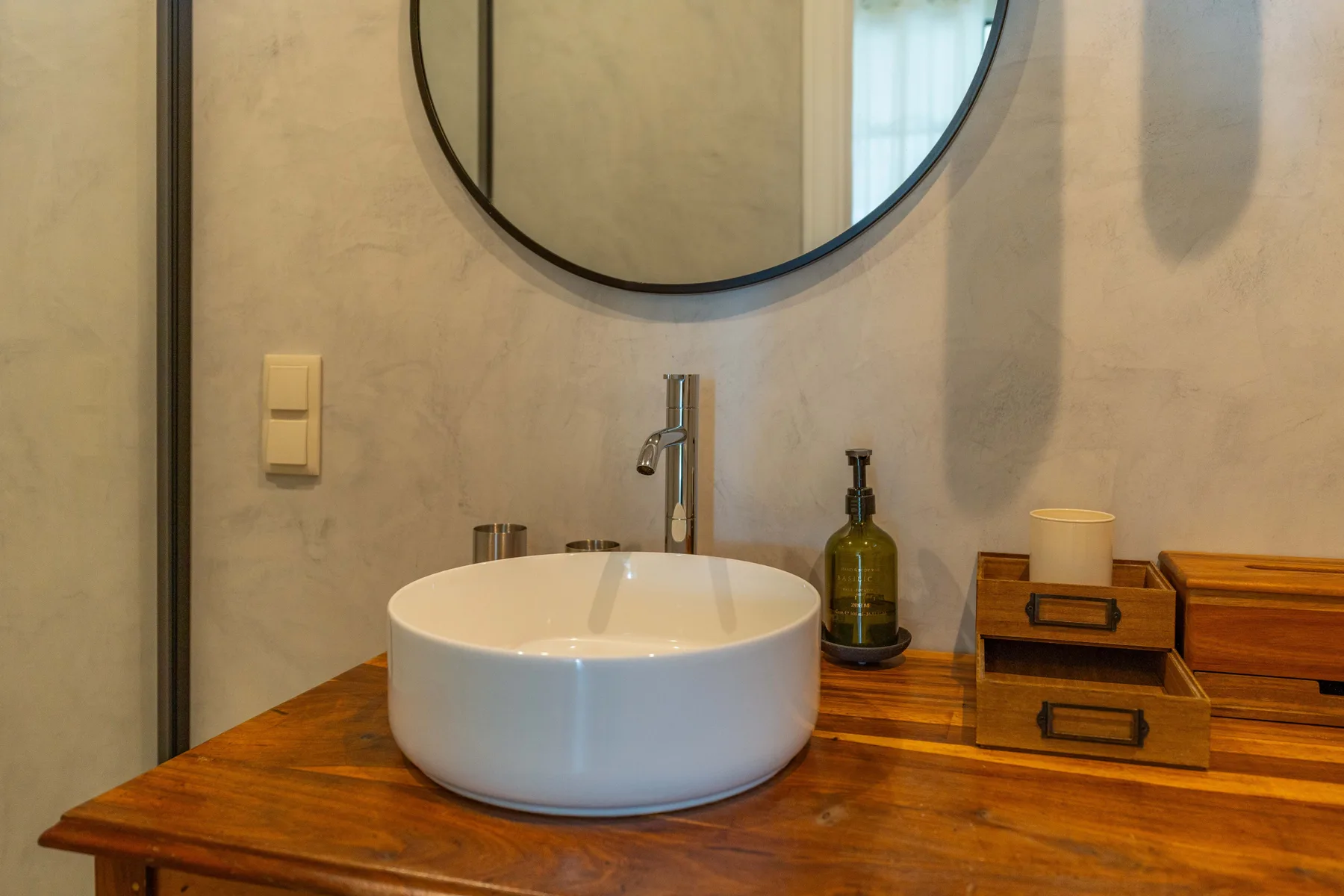 Lavabo de baño con una pila blanca, grifo y espejo redondo.