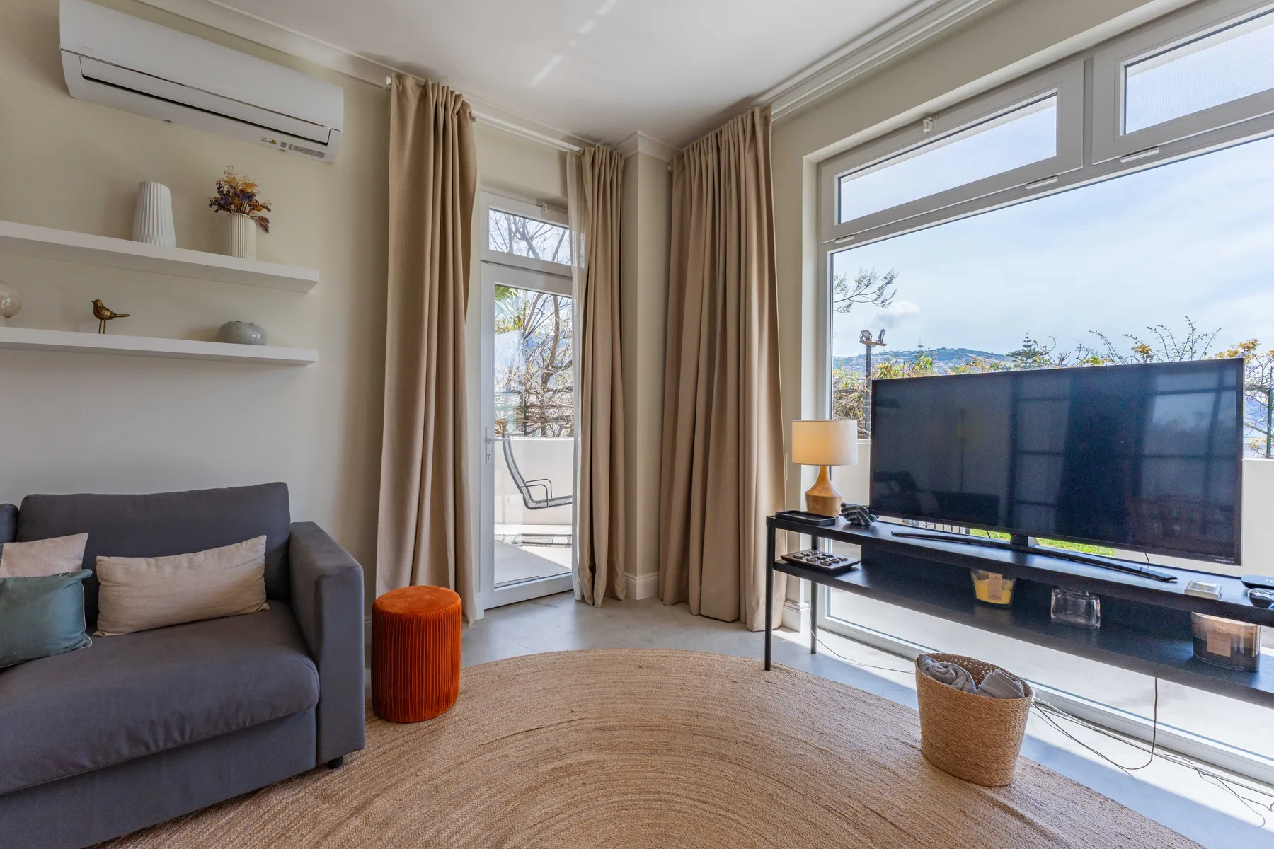 Una sala luminosa con asientos, un televisor y ventanas grandes.