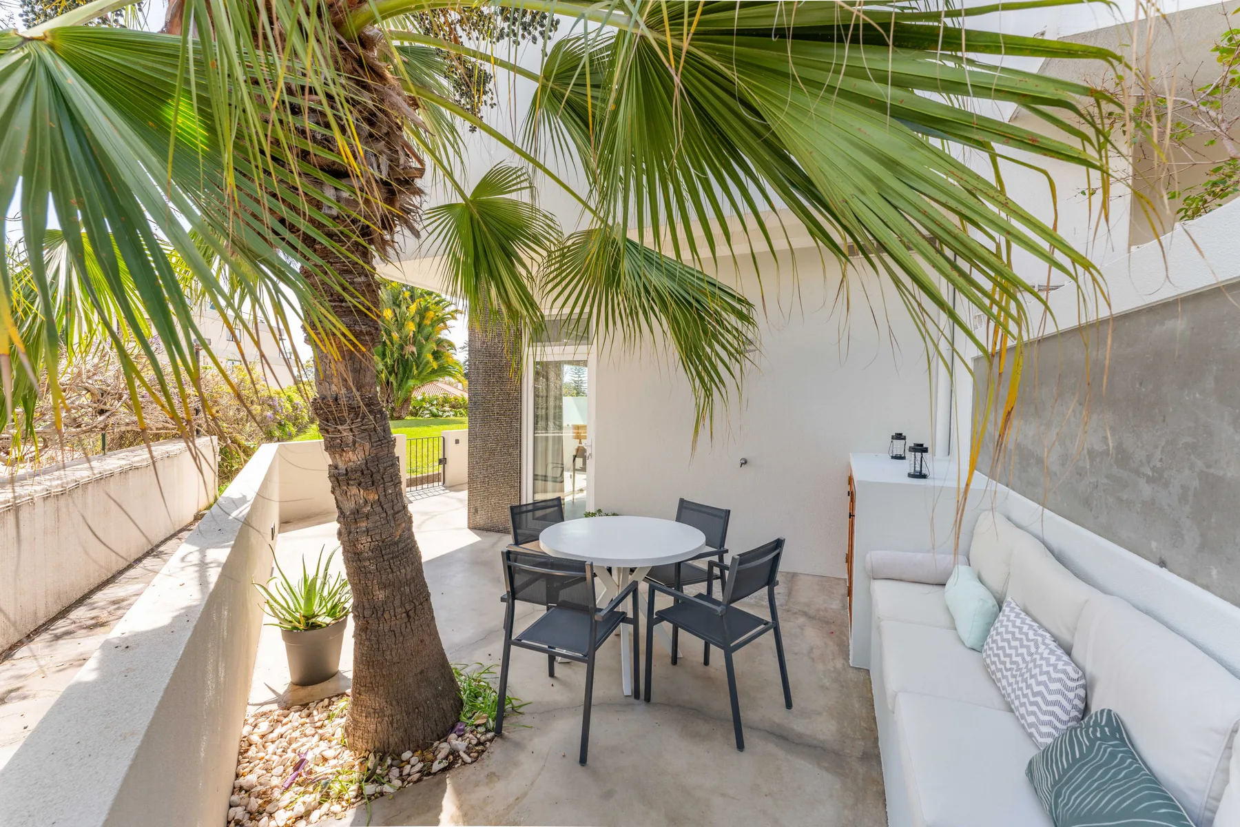 Un patio amueblado con una mesa de comedor y asientos bajo palmeras.