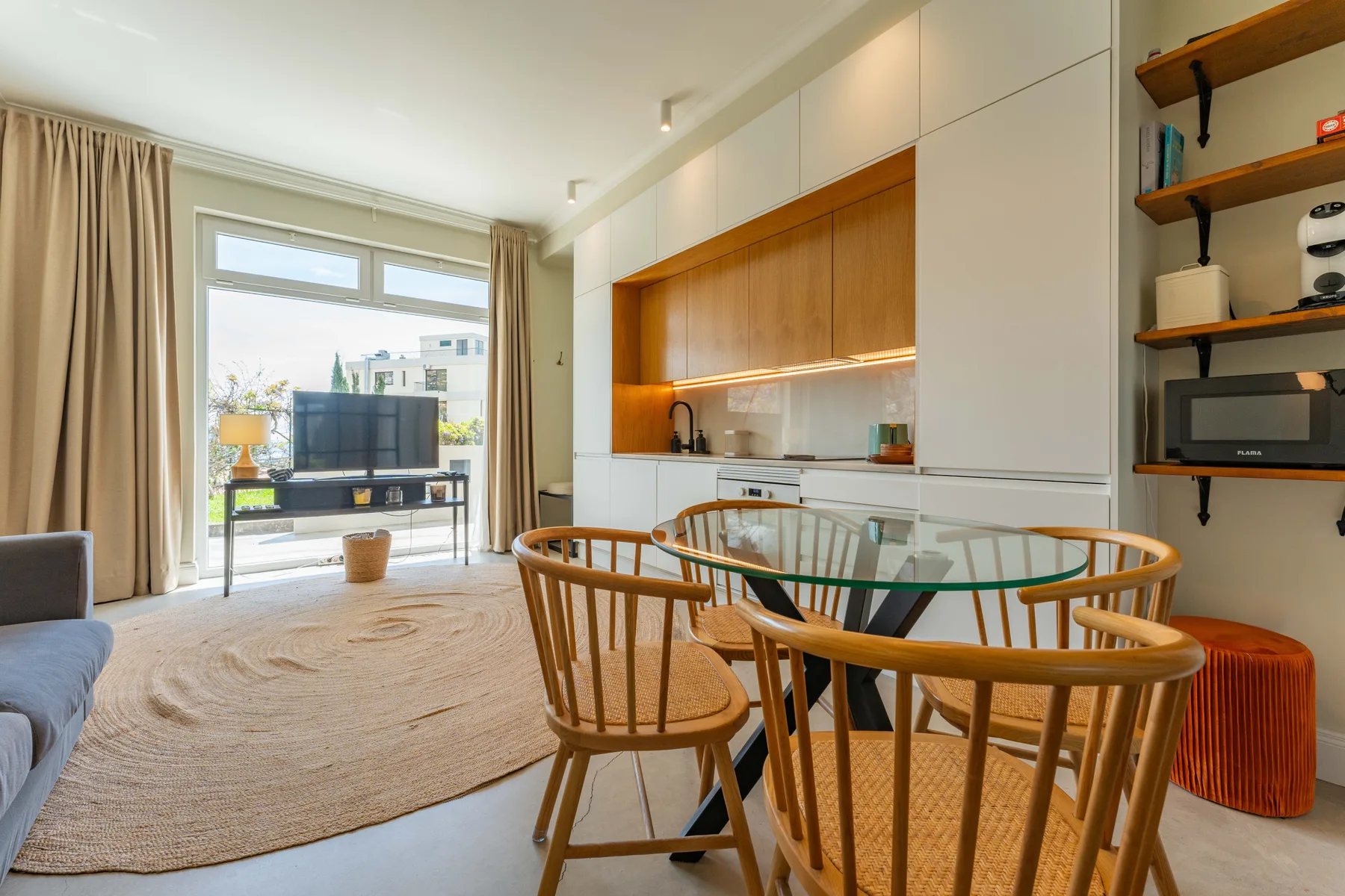 Una luminosa sala de estar y comedor tipo estudio, con mesa de vidrio y asientos junto a las ventanas.