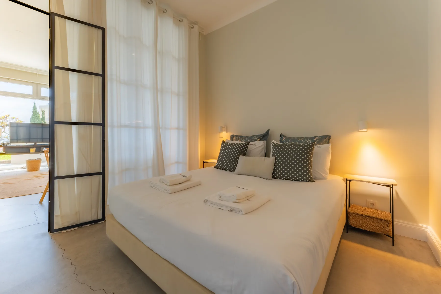 Un dormitorio con una cama bien hecha junto a un separador de paneles de vidrio.