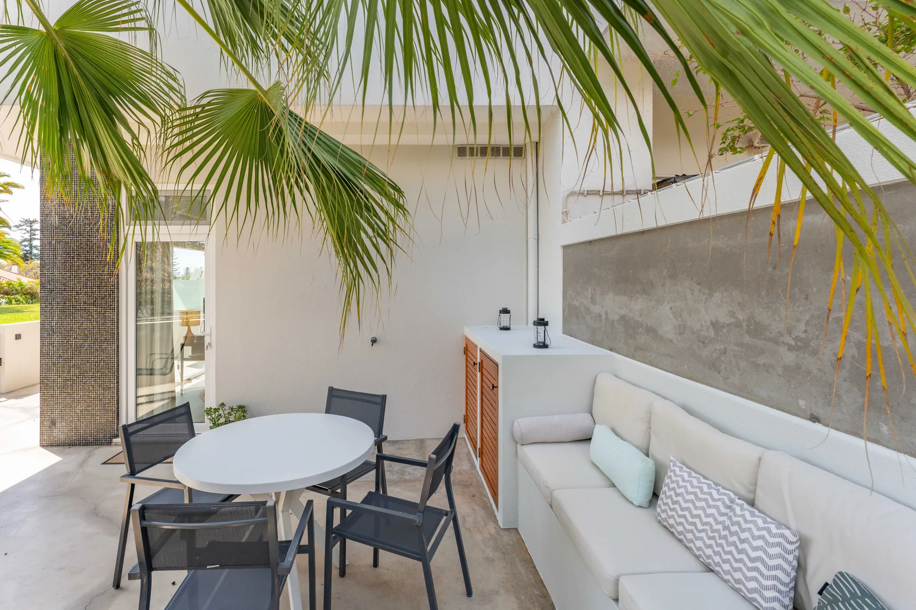 Un patio cubierto con asientos exteriores y un banco largo acolchado junto a una pared.