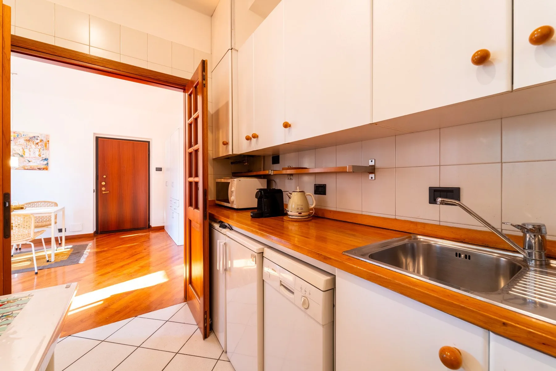 Una cocina luminosa con armarios blancos, encimeras de madera y un fregadero de acero inoxidable.