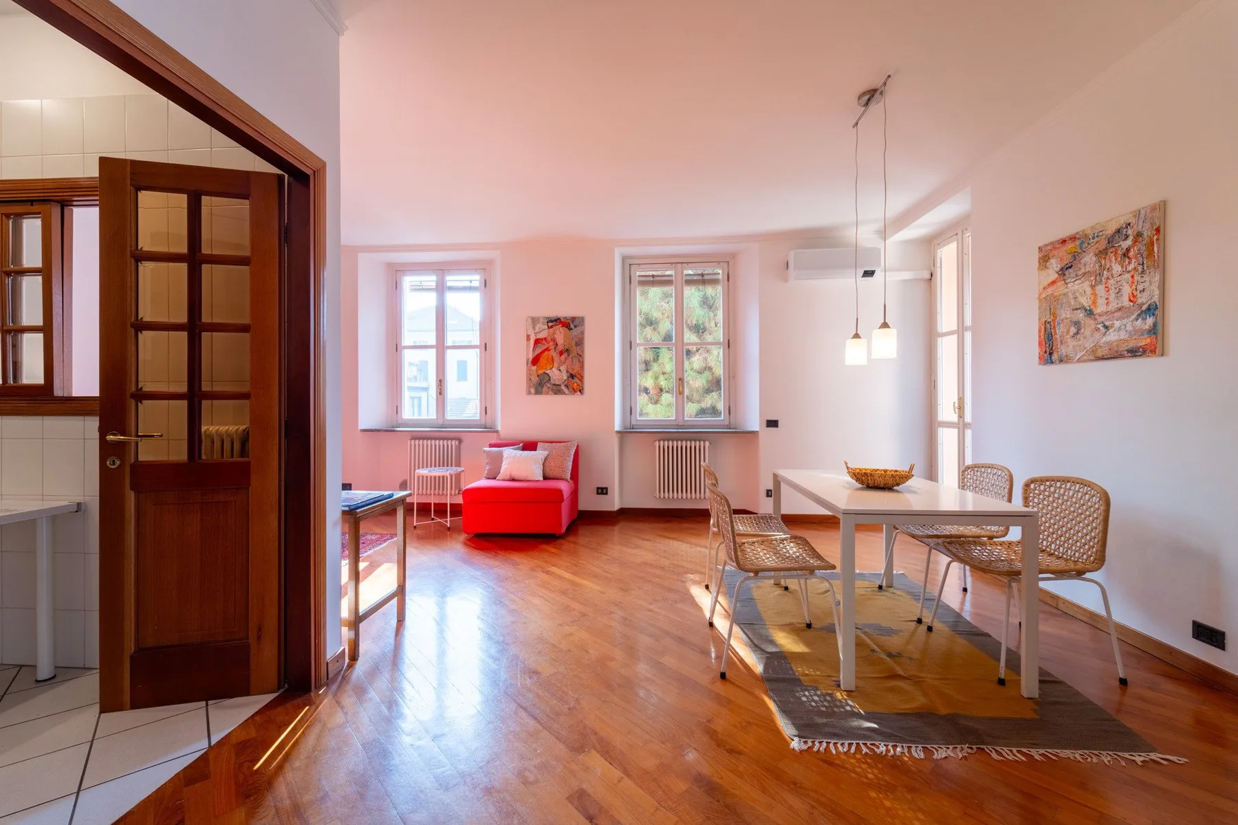 Una luminosa sala de estar y comedor con un asiento rojo y una mesa junto a las ventanas.