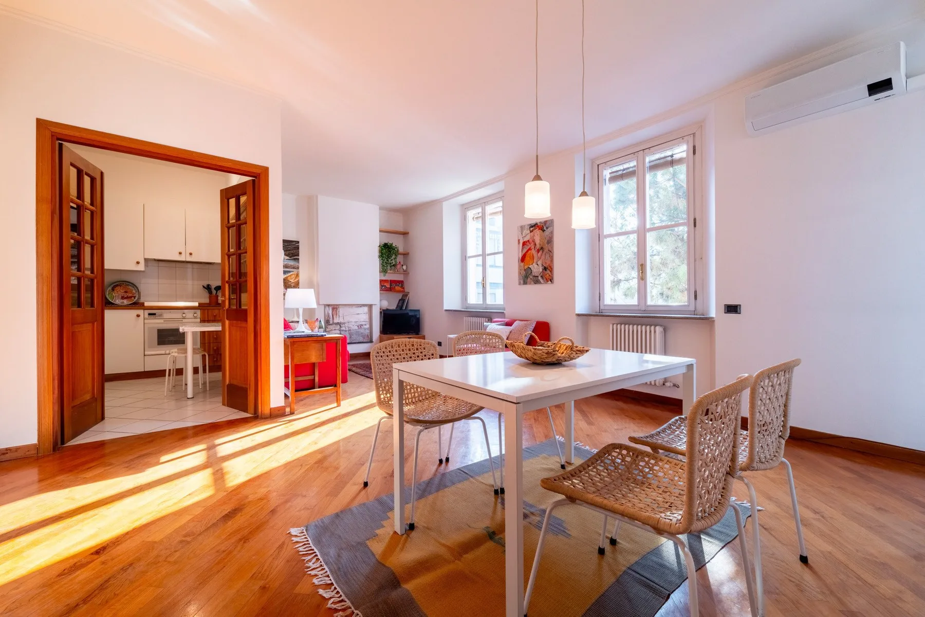 Un comedor luminoso con una mesa y asientos tejidos junto a ventanas altas.