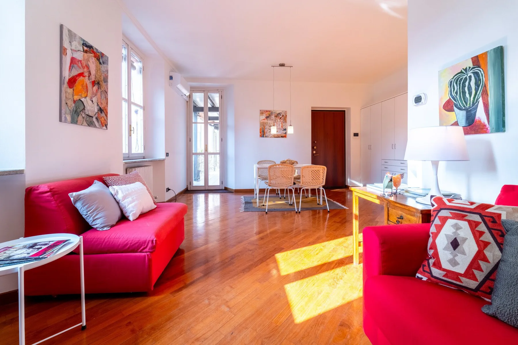 Una sala luminosa con asientos rojos y una mesa de comedor junto a ventanas altas.