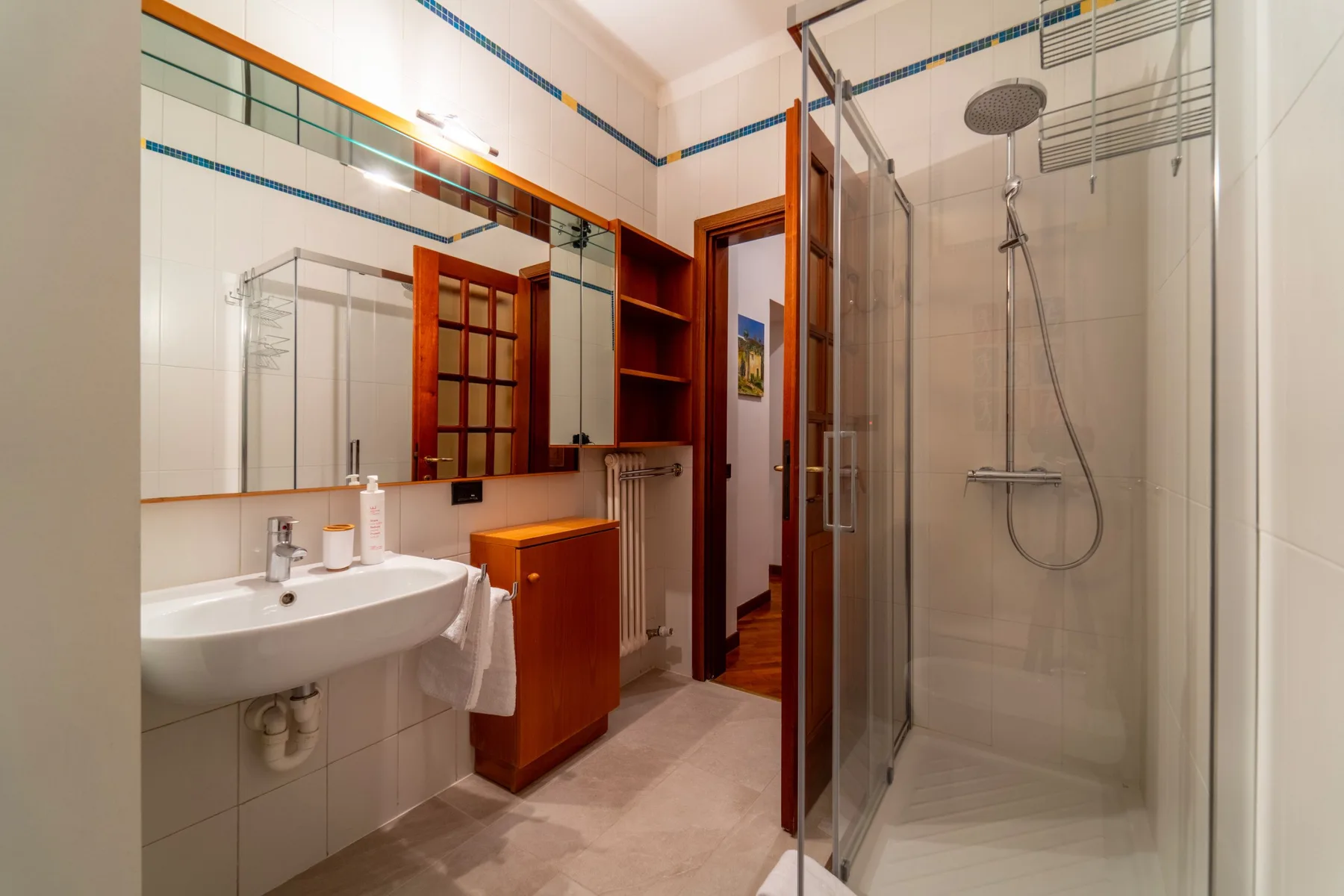 Un baño alicatado con lavabo, muebles de madera y una ducha de cristal.