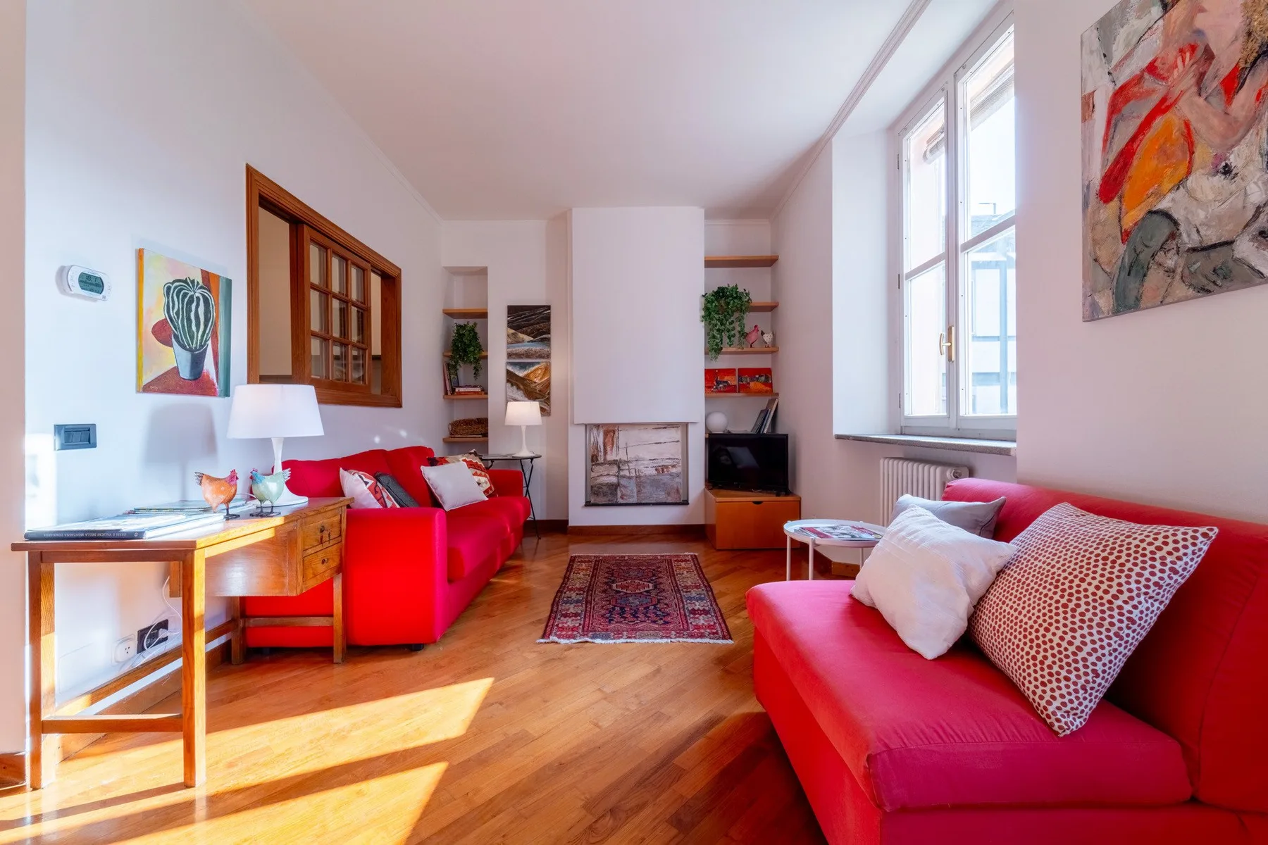 Una sala luminosa con asientos rojos, una chimenea y ventanas altas.